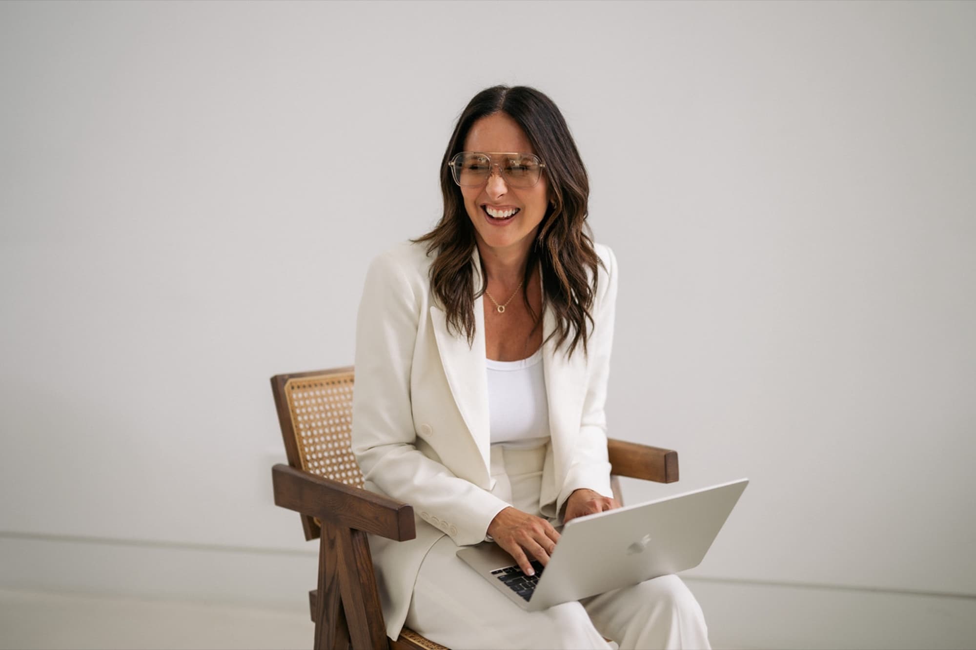 Amy Youngren laughing at her laptop in a white suit